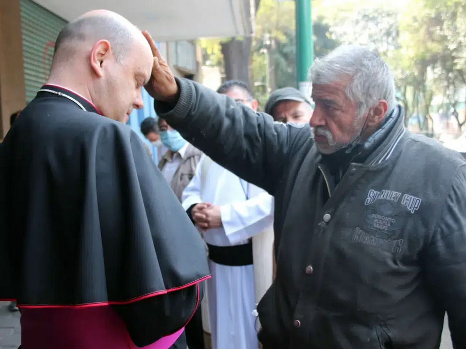 El obispo Francisco Javier Acero recibiendo la bendición de un indigente