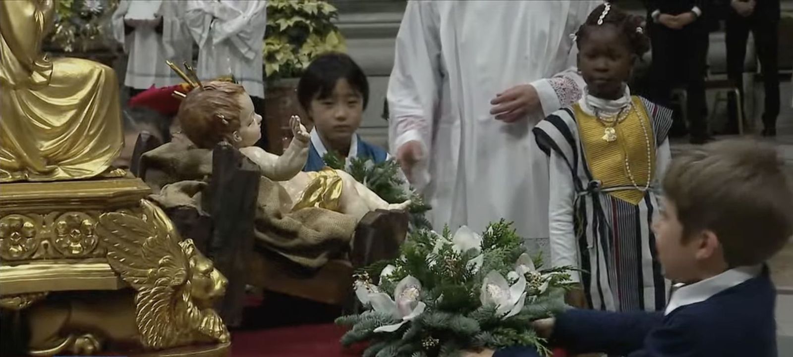 Un grupo de niños ponen flores al niño Dios
